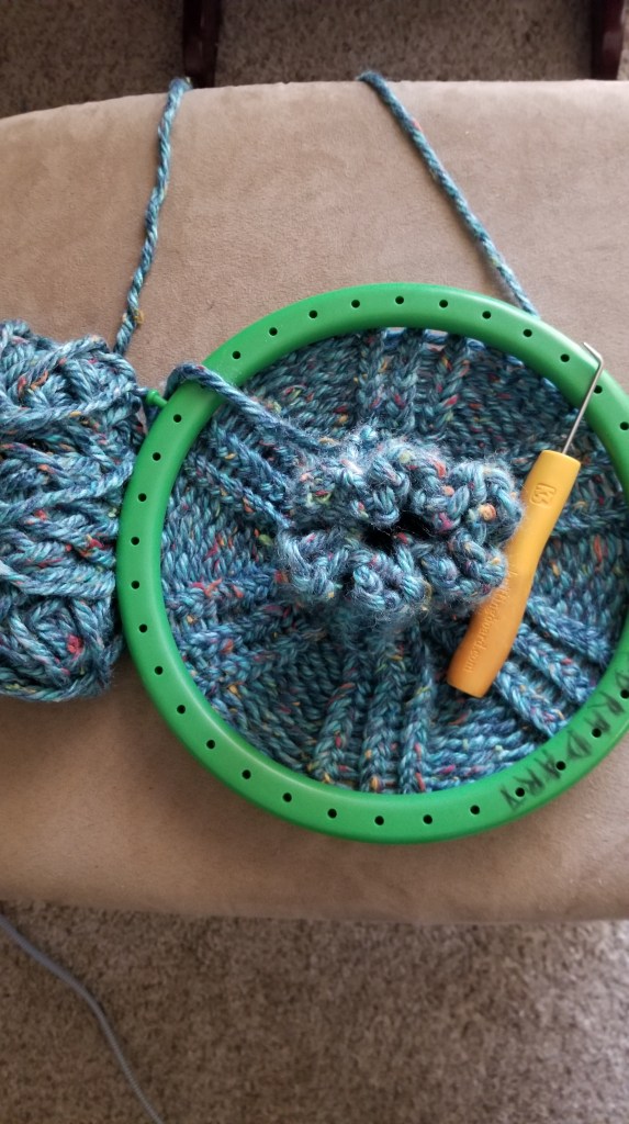 Loom knitting a blue speckled beanie.